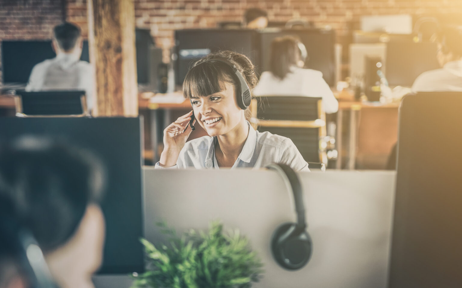 Call center worker accompanied by her team. Smiling customer support operator at work. Young employee working with a headset.