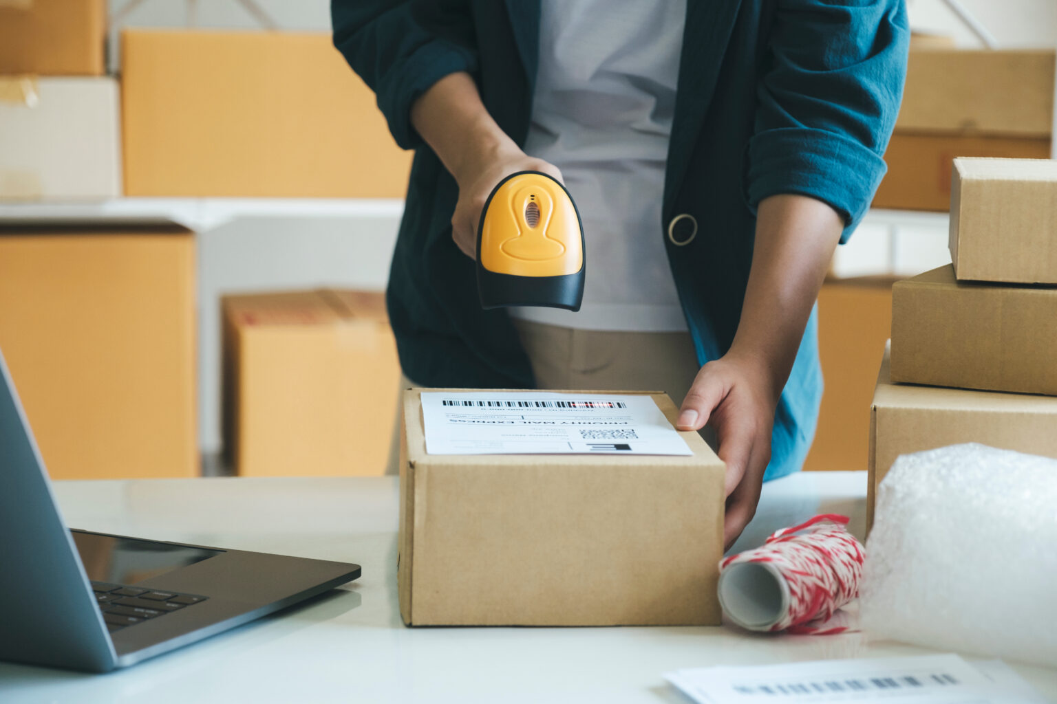 Young entrepreneur scanning online order box. Young female online store seller, owner holding scanner scanning parcel barcode before delivery or shipping to customer. Woman working at factory warehouse scanning labels on the boxes. E-commerce concept.