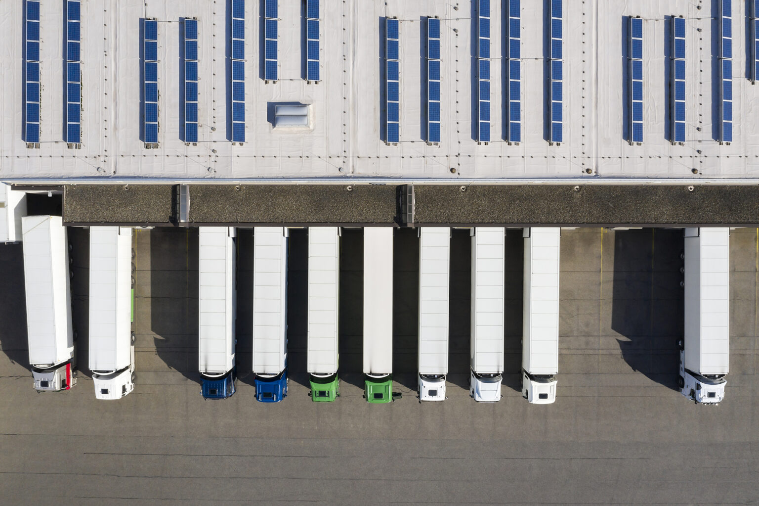 Aerial view of Semi-Trucks Loading at Logistic Center, Distribution Warehouse Aerial view of cargo containers, semi trailers, industrial warehouse, storage building and loading docks, renewable energy plants, Bavaria, Germany