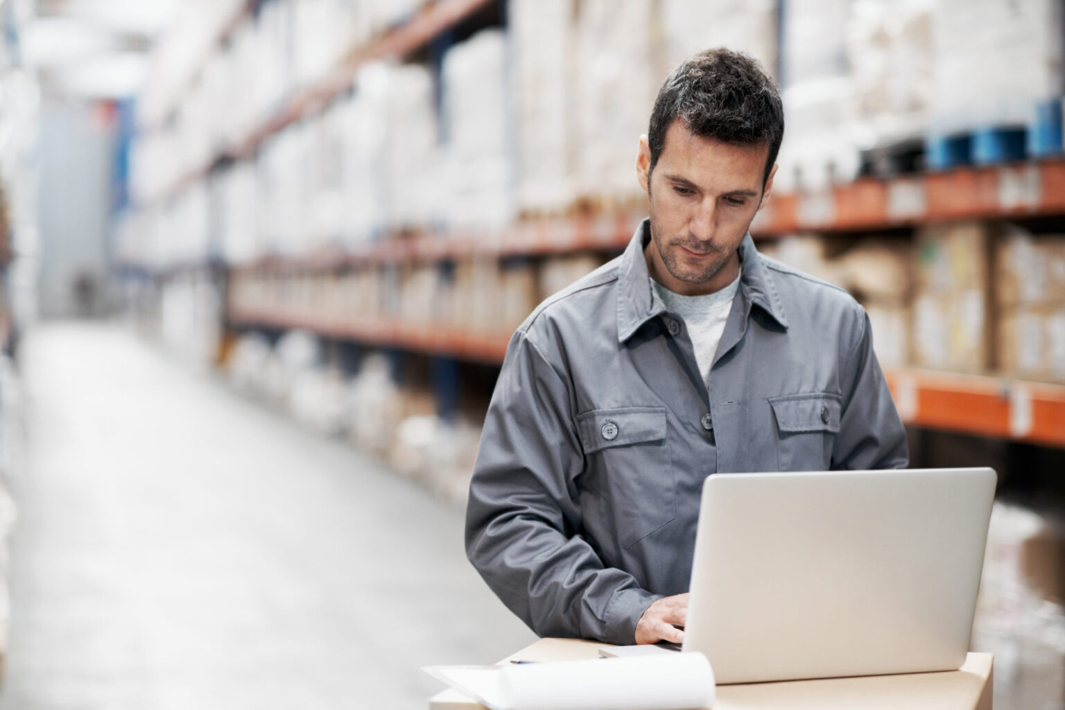 A young man using his notebook and checking his notes while working in a warehouse