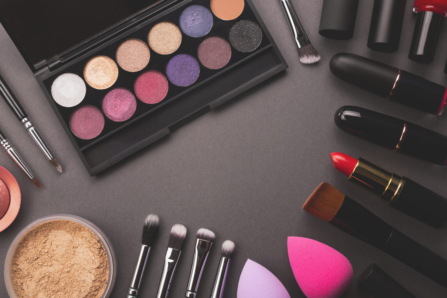Makeup moody frame background. Decorative cosmetic flat lay including eye shadows palette, foundation, brushes and tools. Beauty concept. Top view, copy space.