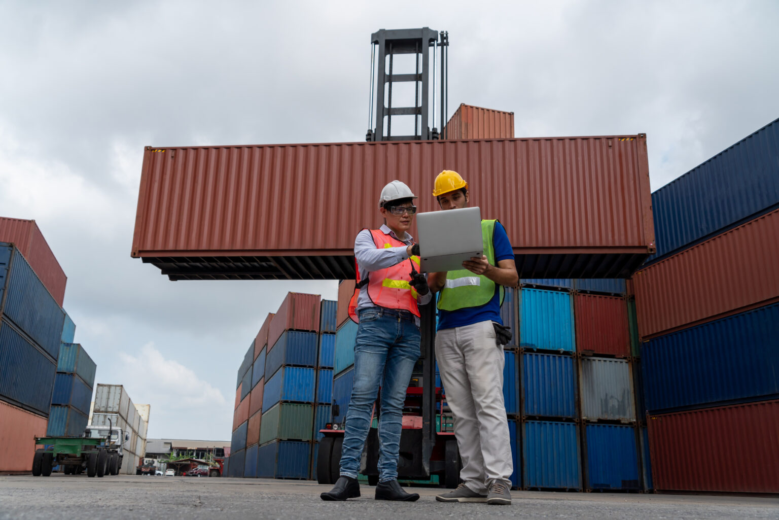 Industrial worker works with co-worker at overseas shipping container yard . Logistics supply chain management and international goods export concept .