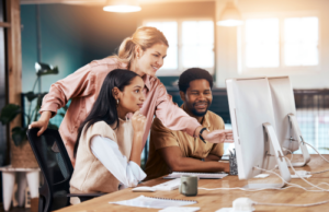 Business team, computer and happy mentor talking to people at office desk for motivation.